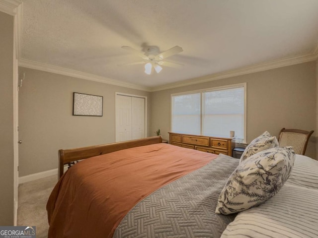 carpeted bedroom featuring baseboards, ceiling fan, a closet, and crown molding