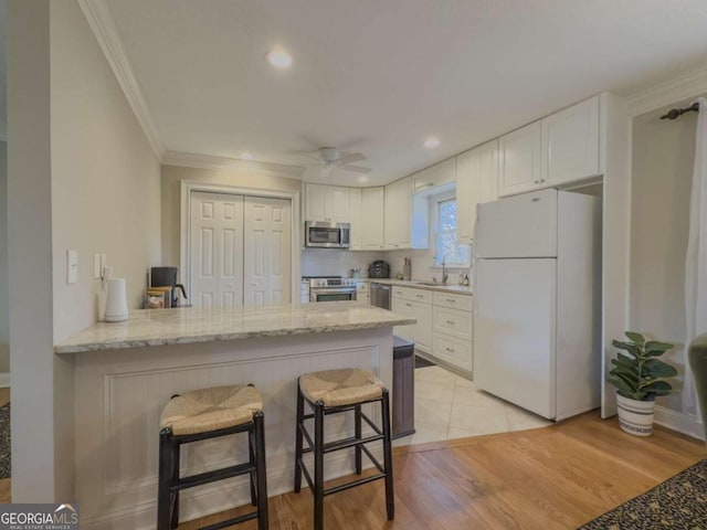 kitchen featuring stainless steel appliances, a peninsula, a sink, and white cabinetry