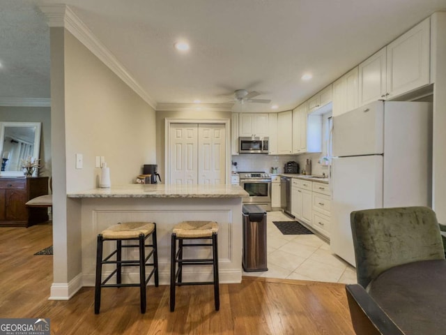 kitchen featuring a peninsula, a kitchen breakfast bar, white cabinets, appliances with stainless steel finishes, and crown molding