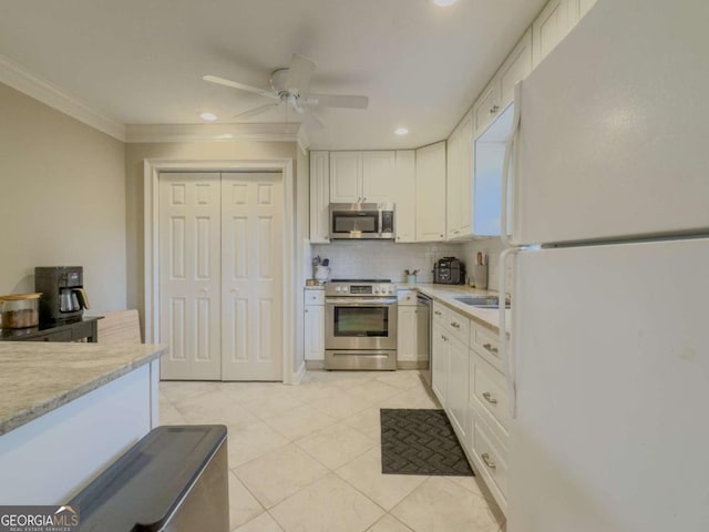 kitchen with light tile patterned floors, white cabinets, stainless steel appliances, crown molding, and backsplash