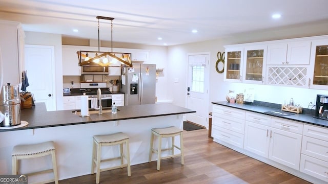 kitchen with appliances with stainless steel finishes, dark countertops, glass insert cabinets, and light wood finished floors