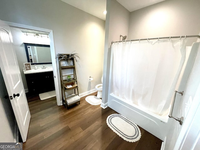 bathroom with baseboards, toilet, wood finished floors, shower / bathtub combination with curtain, and vanity