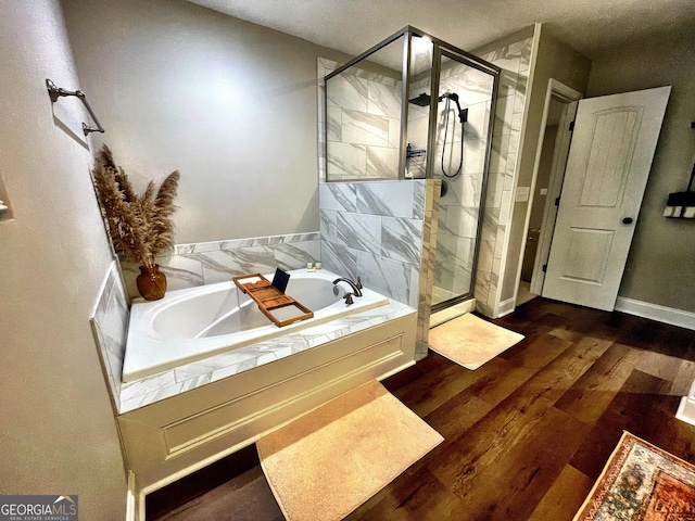 bathroom featuring a stall shower, a garden tub, baseboards, and wood finished floors