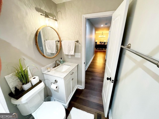 half bathroom with visible vents, toilet, wood finished floors, an inviting chandelier, and vanity