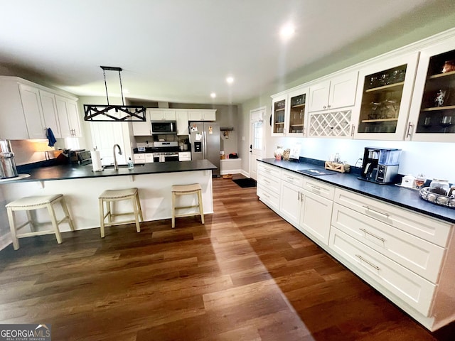 kitchen with dark countertops, glass insert cabinets, dark wood-style flooring, a peninsula, and stainless steel appliances