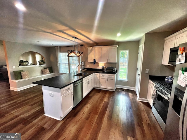 kitchen featuring a peninsula, a sink, white cabinets, appliances with stainless steel finishes, and dark countertops