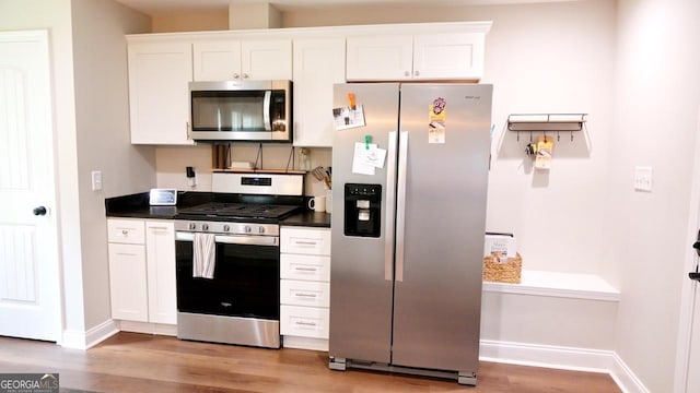 kitchen with stainless steel appliances, light wood finished floors, dark countertops, and white cabinetry