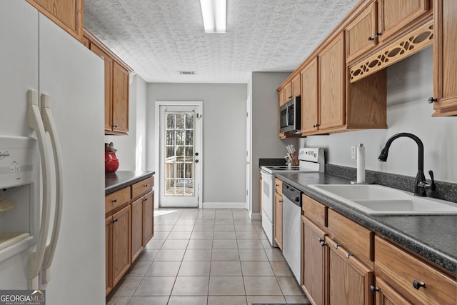 kitchen with light tile patterned floors, dark countertops, appliances with stainless steel finishes, a textured ceiling, and a sink