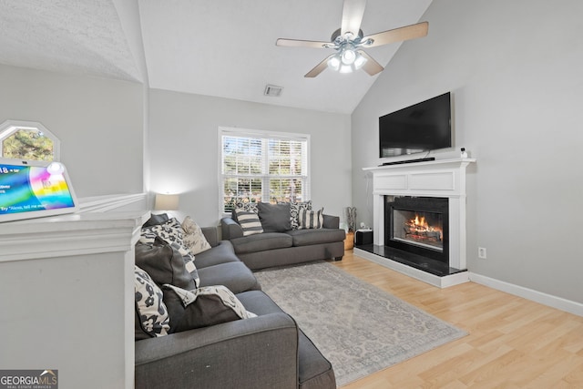 living room featuring ceiling fan, wood finished floors, visible vents, baseboards, and a glass covered fireplace