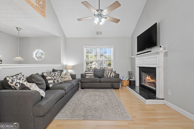 living room featuring baseboards, visible vents, a glass covered fireplace, lofted ceiling, and wood finished floors