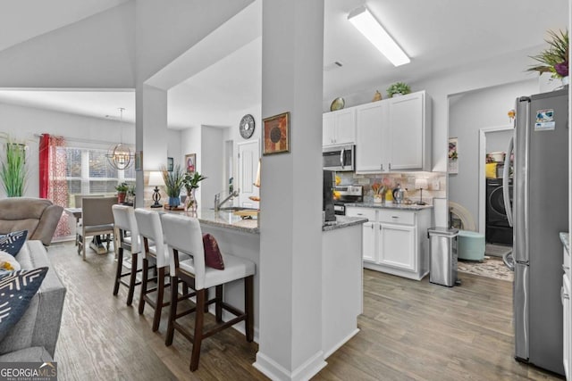 kitchen with light stone counters, wood finished floors, white cabinetry, appliances with stainless steel finishes, and a kitchen bar