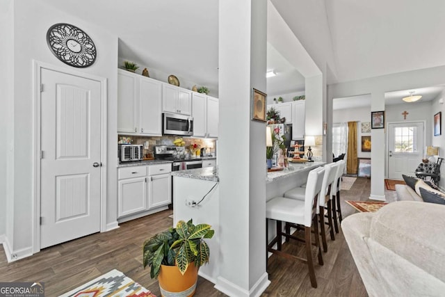 kitchen featuring white cabinets, appliances with stainless steel finishes, a kitchen breakfast bar, dark wood-style flooring, and backsplash