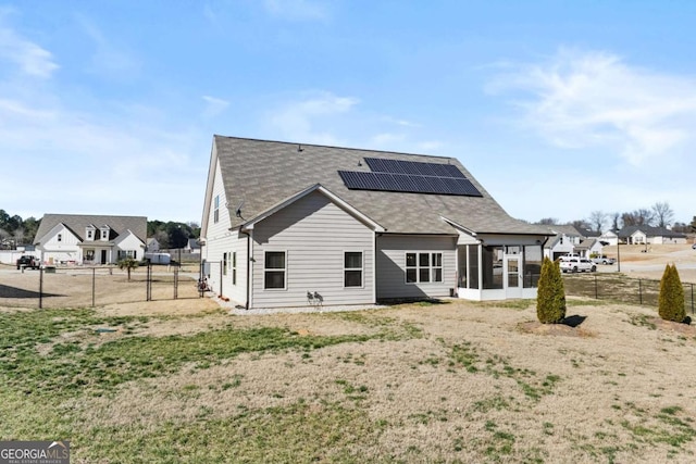 rear view of property with fence, a sunroom, and roof mounted solar panels