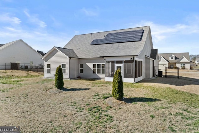 rear view of property featuring a lawn, a sunroom, roof mounted solar panels, a gate, and a fenced backyard