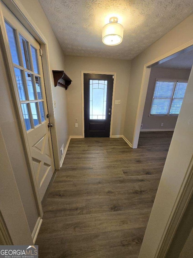 foyer entrance with a textured ceiling, dark wood-type flooring, visible vents, and baseboards