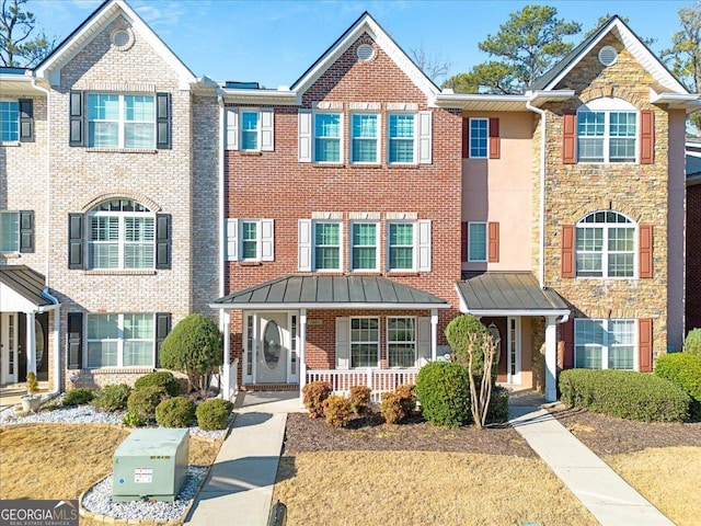 townhome / multi-family property featuring metal roof, covered porch, brick siding, stone siding, and a standing seam roof