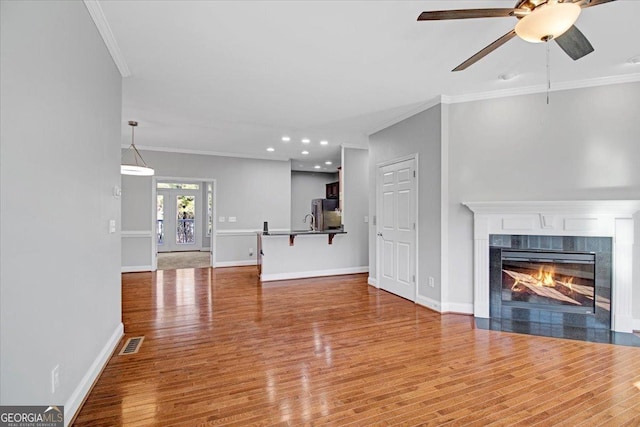 unfurnished living room featuring ornamental molding, a tile fireplace, visible vents, and wood finished floors