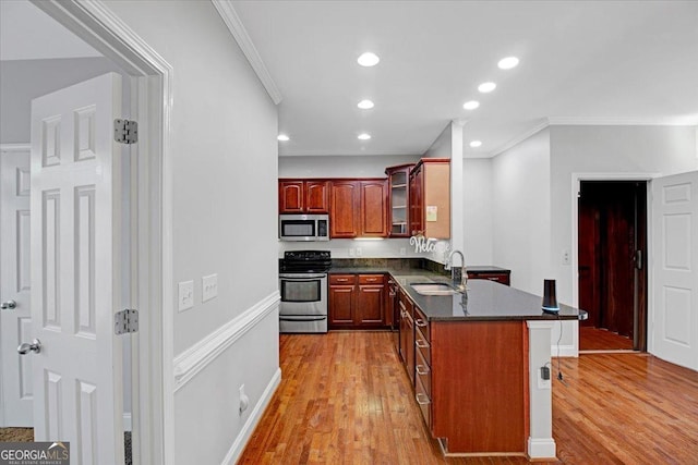 kitchen featuring appliances with stainless steel finishes, glass insert cabinets, a peninsula, crown molding, and a sink