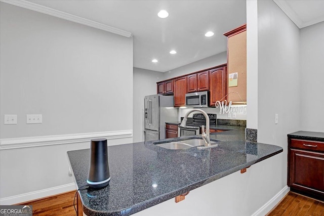 kitchen with appliances with stainless steel finishes, ornamental molding, dark wood-style flooring, a peninsula, and a sink