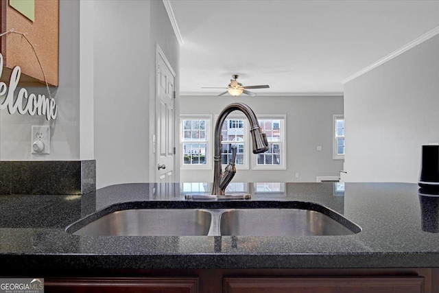 kitchen featuring crown molding, a ceiling fan, dark stone counters, and a sink