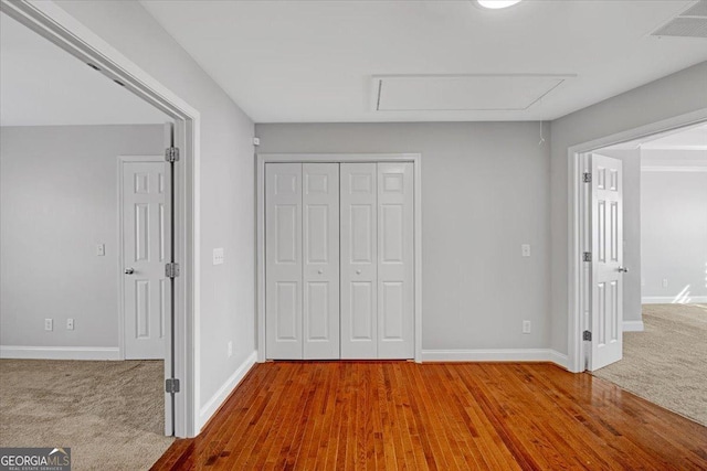 unfurnished bedroom featuring wood finished floors, carpet flooring, visible vents, baseboards, and a closet