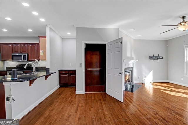 kitchen with a breakfast bar, stainless steel microwave, black electric range oven, a sink, and wood finished floors