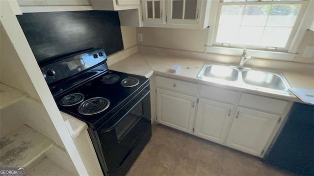 kitchen with a sink, white cabinets, light countertops, black electric range oven, and glass insert cabinets