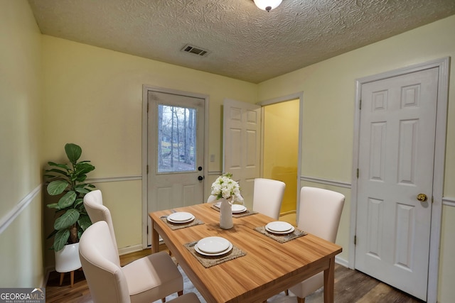 dining area with a textured ceiling, dark wood-type flooring, and visible vents