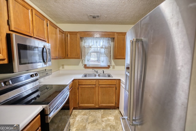 kitchen featuring brown cabinetry, visible vents, stainless steel appliances, and a sink