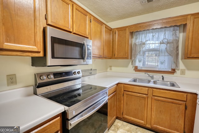 kitchen with a textured ceiling, a sink, light countertops, appliances with stainless steel finishes, and brown cabinets