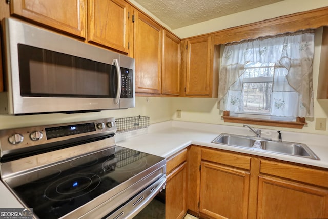 kitchen featuring appliances with stainless steel finishes, light countertops, a sink, and a textured ceiling