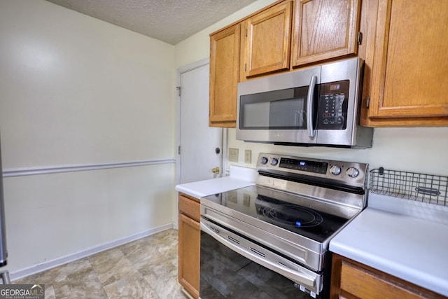 kitchen featuring baseboards, appliances with stainless steel finishes, brown cabinets, light countertops, and a textured ceiling