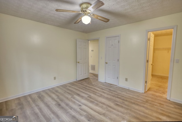 unfurnished bedroom featuring a walk in closet, visible vents, light wood-style floors, a textured ceiling, and baseboards