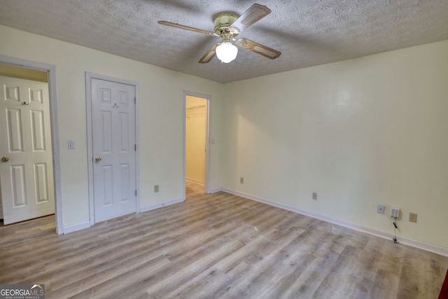 unfurnished bedroom with a textured ceiling, a ceiling fan, baseboards, light wood-type flooring, and a walk in closet