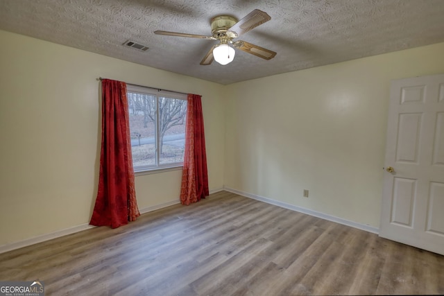 unfurnished room featuring a textured ceiling, wood finished floors, a ceiling fan, visible vents, and baseboards