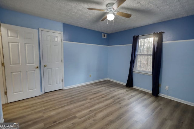 unfurnished bedroom with baseboards, a textured ceiling, visible vents, and wood finished floors