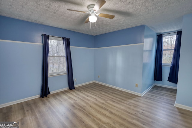 empty room featuring a ceiling fan, a textured ceiling, baseboards, and wood finished floors