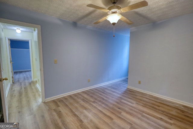 empty room featuring a textured ceiling, wood finished floors, a ceiling fan, and baseboards