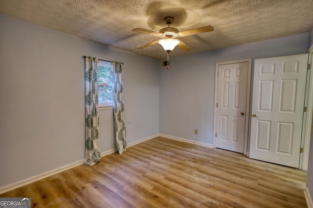 unfurnished bedroom with ceiling fan, light wood-style flooring, baseboards, and a textured ceiling