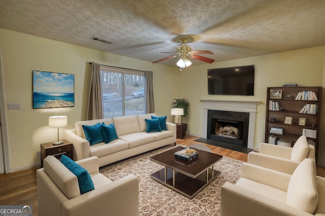 living room featuring visible vents, ceiling fan, wood finished floors, a textured ceiling, and a fireplace