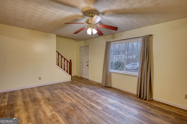 spare room featuring a ceiling fan, baseboards, stairway, and wood finished floors