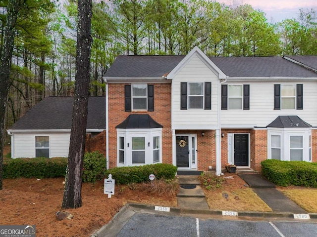 view of front of home featuring uncovered parking, brick siding, and a shingled roof