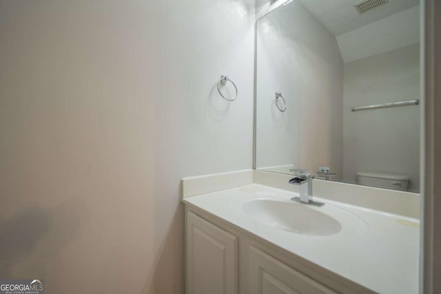 bathroom with toilet, visible vents, vaulted ceiling, and vanity