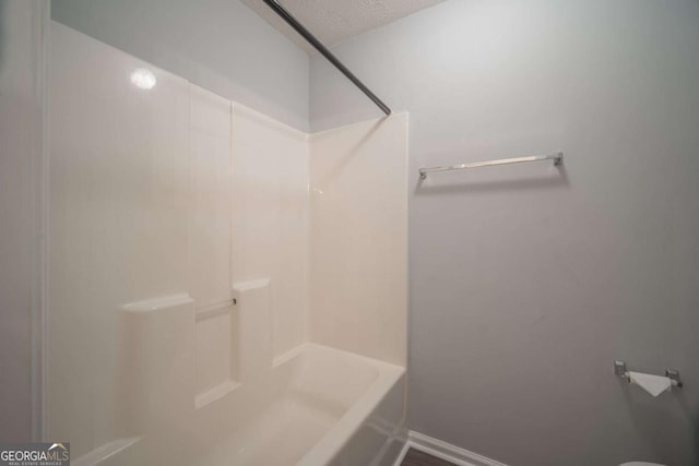 full bathroom featuring a textured ceiling and baseboards