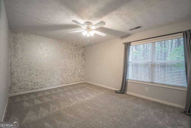 carpeted spare room featuring baseboards, ceiling fan, visible vents, and a textured ceiling