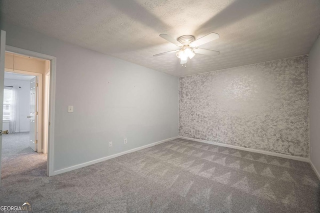 carpeted spare room with a textured ceiling, ceiling fan, and attic access