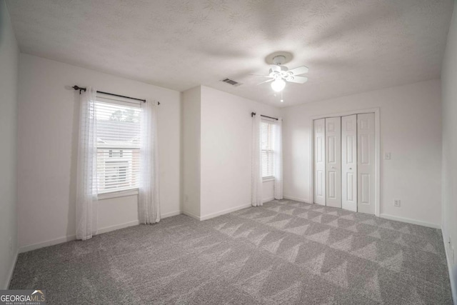 unfurnished bedroom featuring a textured ceiling, carpet, visible vents, and baseboards