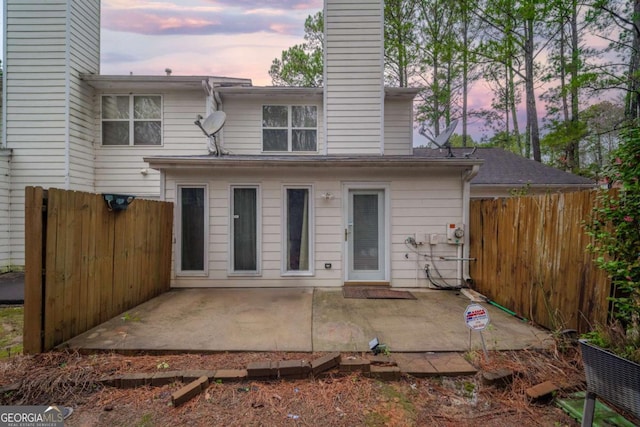 back of property at dusk featuring a patio, a chimney, and fence