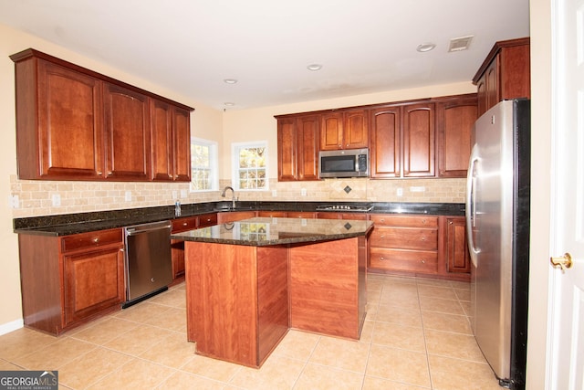 kitchen featuring dark stone counters, decorative backsplash, a center island, stainless steel appliances, and light tile patterned flooring