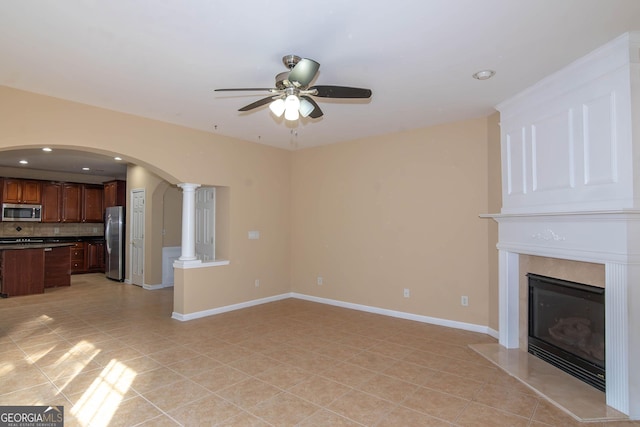 unfurnished living room featuring light tile patterned floors, baseboards, arched walkways, a ceiling fan, and a high end fireplace